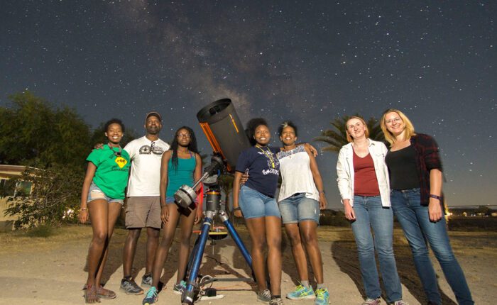 A group of diverse young people stargazing with a telescope under a starry night.