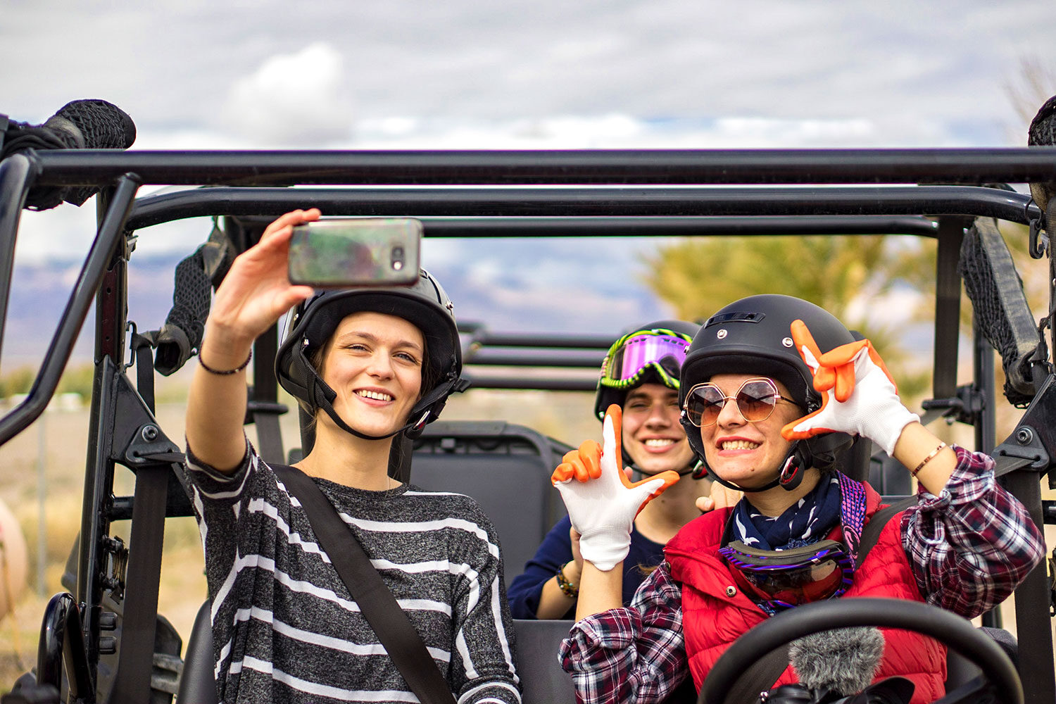 Three smiling helmeted women in an ATV taking a selfie.