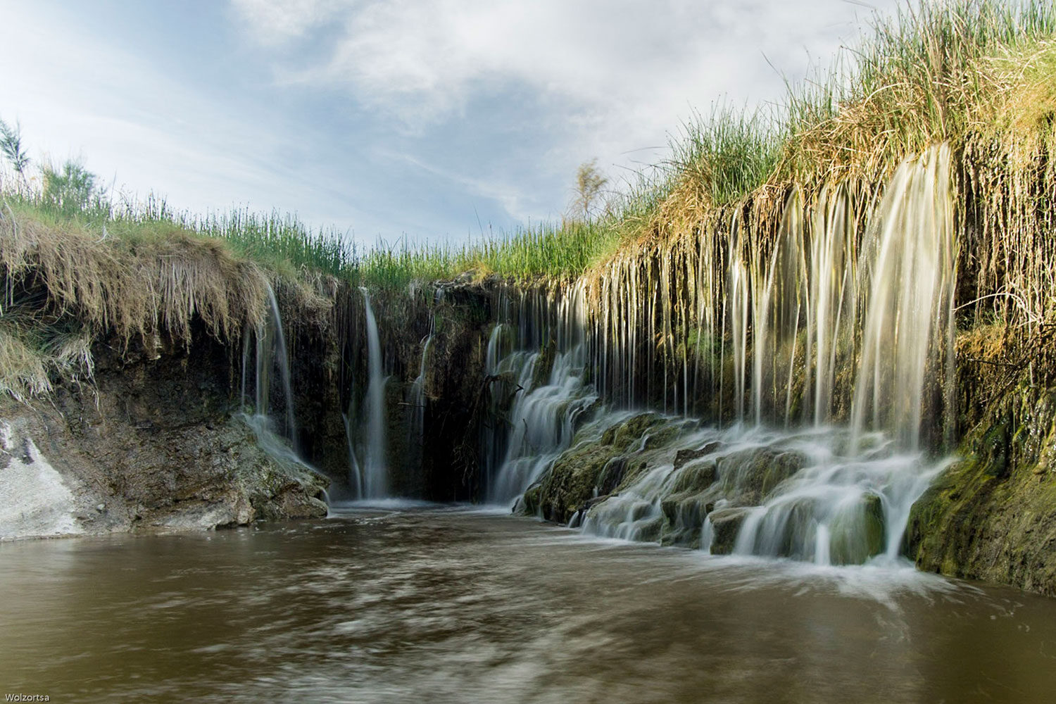 Waterfall flowing over a grassy edge.