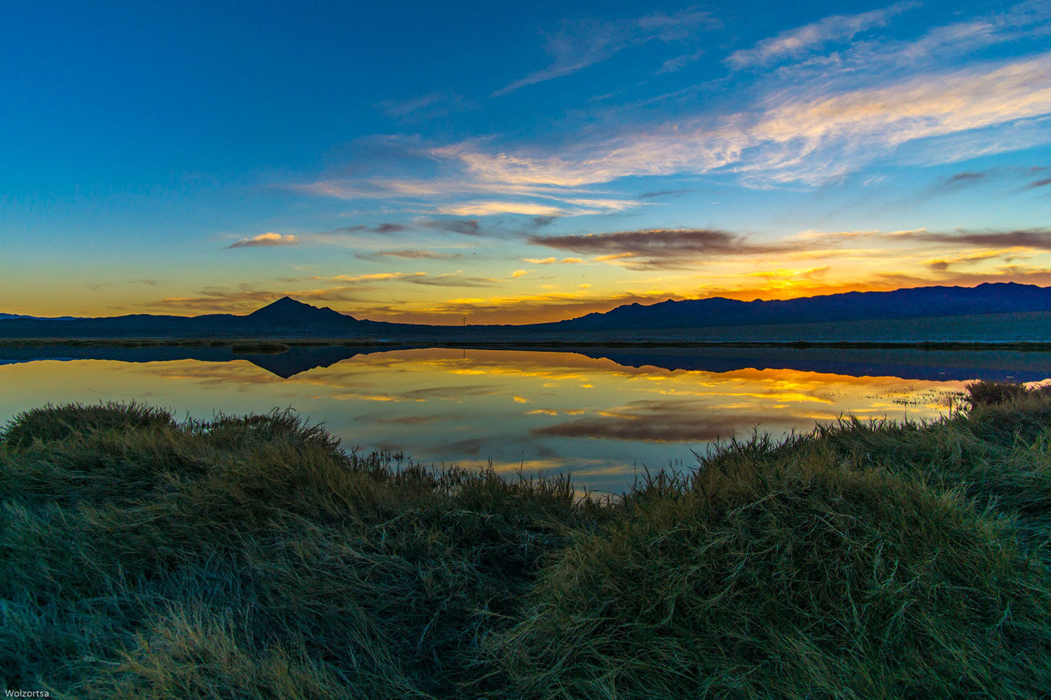 A lake surrounded by mountains during a colorful sunset in a remote desert region.