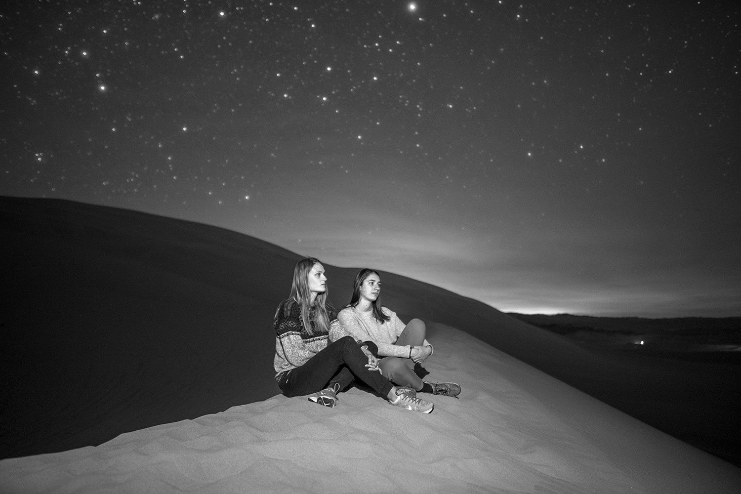 Two contemplative women on top a sand dune at night.
