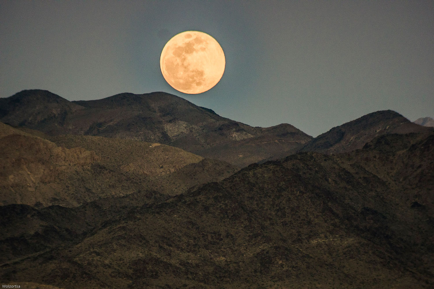 Moon rise cresting a desert mountain range.