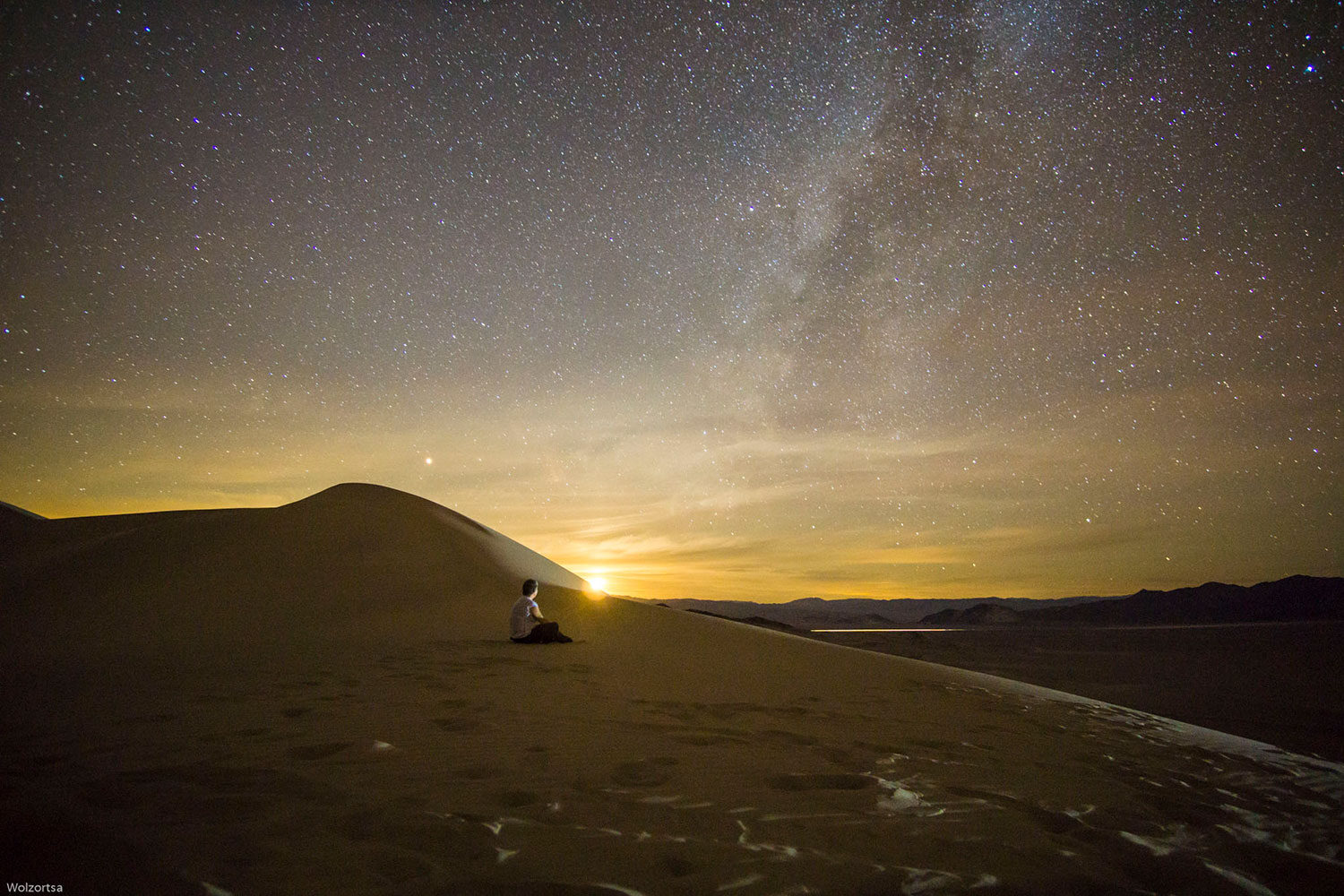 A person sitting cross-legged atop a sand dune contemplating the milky way.
