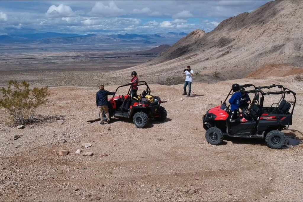 Two ATVs with men and women stopped on a desert overlook with one taking pictures