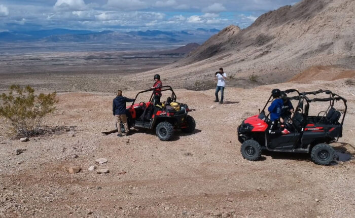 Two ATVs with men and women stopped on a desert overlook with one taking pictures