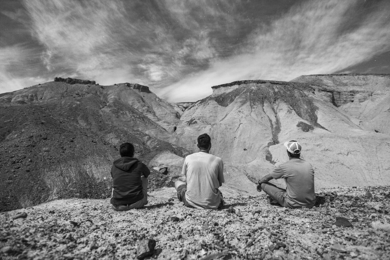 Three people sitting on a rocky cliff overlooking a dramatic mountainous landscape with cloudy skies. Three people sitting on a rocky cliff overlooking a dramatic mountainous landscape with cloudy skies.