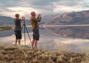 Two photographers capturing a serene mountain lake at sunrise.