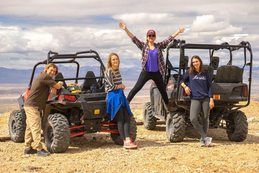 Four friends posing happily beside off-road vehicles on a cloudy day.