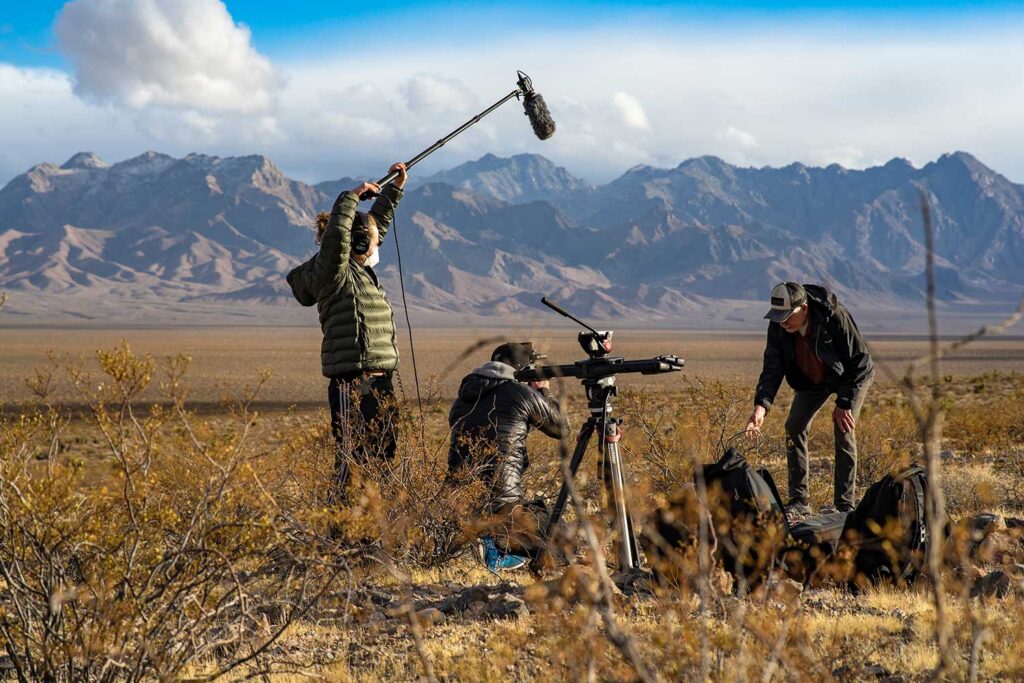 Three men with sound and film equipment working in the desert