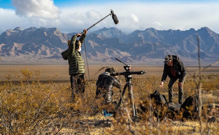 Three men with sound and film equipment working in the desert